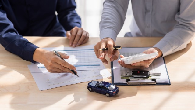 Two people discussing finances over paperwork, a toy car, calculator, and car keys on a wooden table.