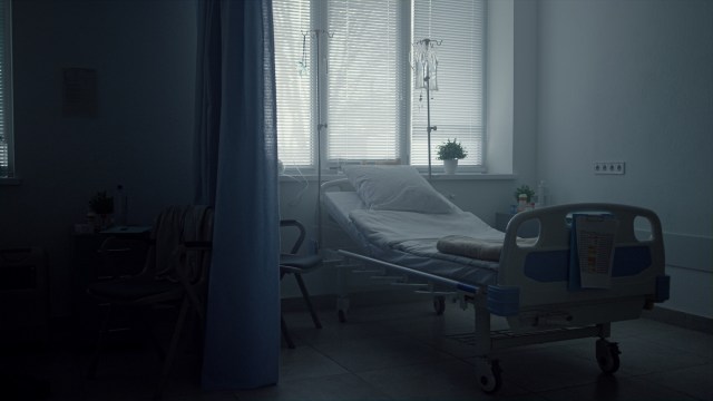 A hospital room with a bed, IV stand, and a chair near a window.