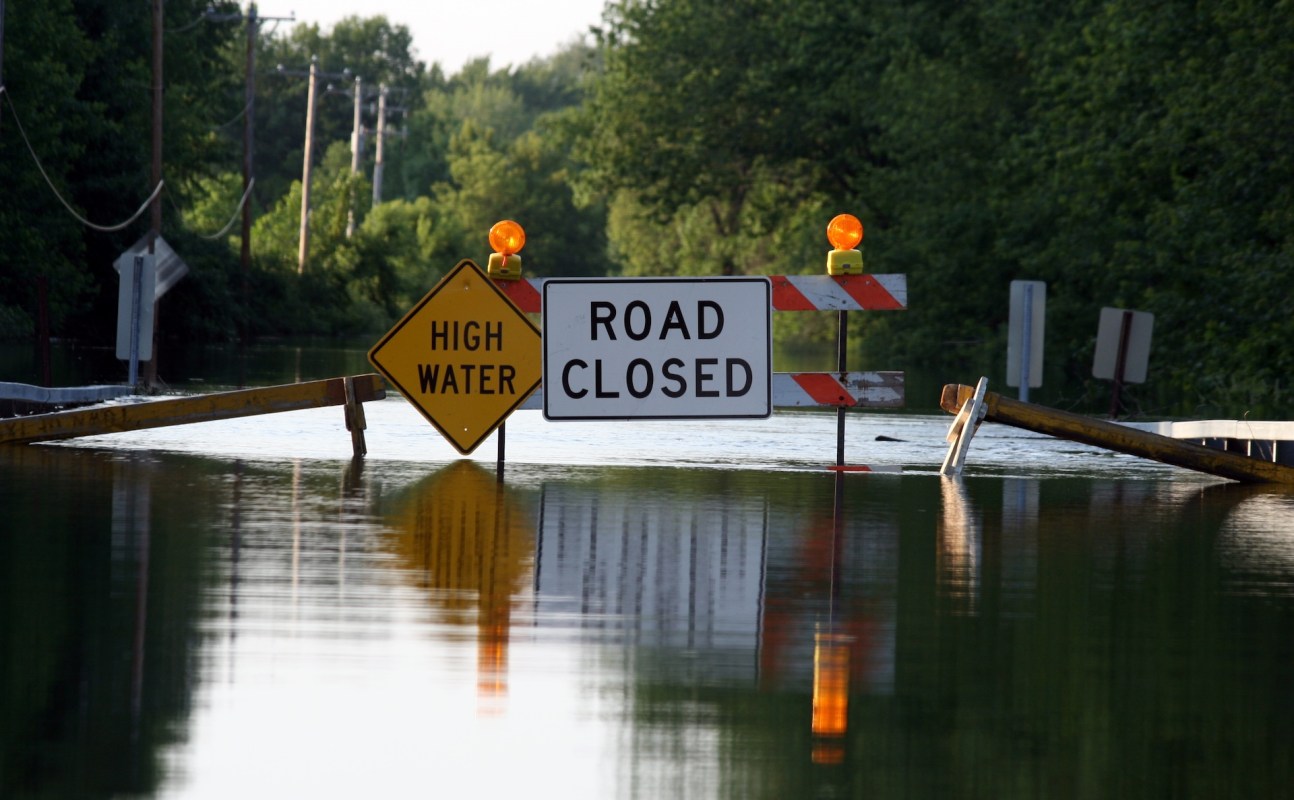 A flooded road with "High Water" and "Road Closed" warning signs.
