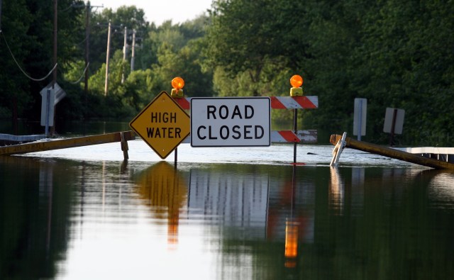 A flooded road with "High Water" and "Road Closed" warning signs.