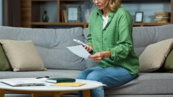 A woman with a smartphone reviewing documents in a living room.