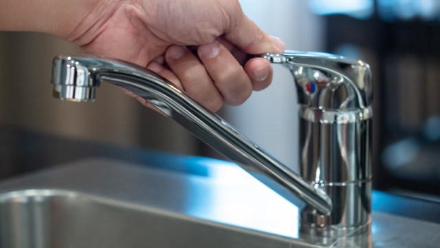 A person adjusting a kitchen faucet.