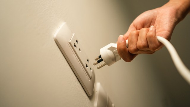 A person unplugging an electrical cord from a wall outlet.