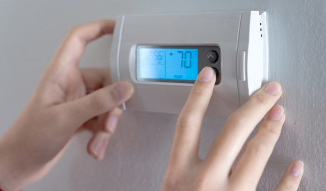 A person adjusts a digital thermostat displaying 70°F on a wall.