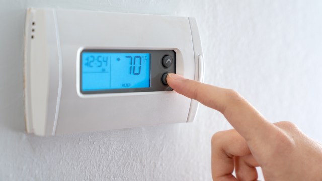 A person adjusts a digital thermostat displaying a temperature of 70°F.