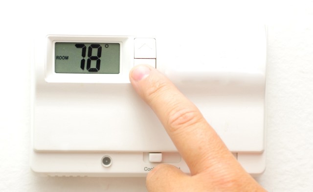 A hand adjusting a digital thermostat displaying a room temperature of 78 degrees Fahrenheit.