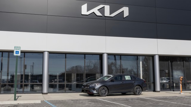 A gray sedan outside a Kia dealership.