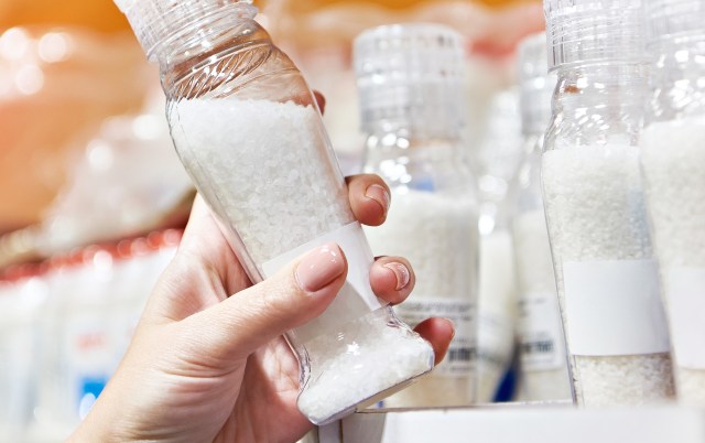 A hand holding a clear salt shaker in a grocery store.