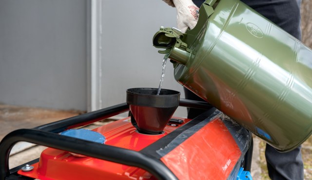 A person pours liquid from a green container into a black funnel on a red generator.