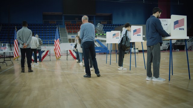 Voters cast their ballots at polling stations in a gym decorated with U.S. flags on a voting day.