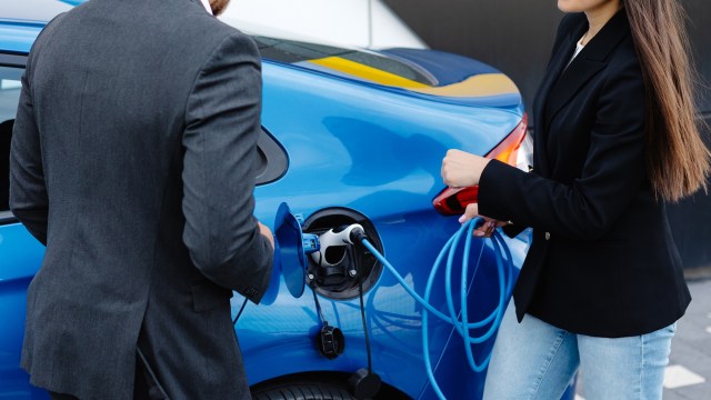 Two people next to a charging electric vehicle.
