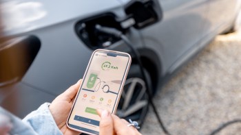A person views a smartphone displaying charging information for an electric vehicle.