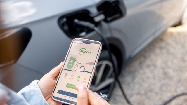 A person views a smartphone displaying charging information for an electric vehicle.