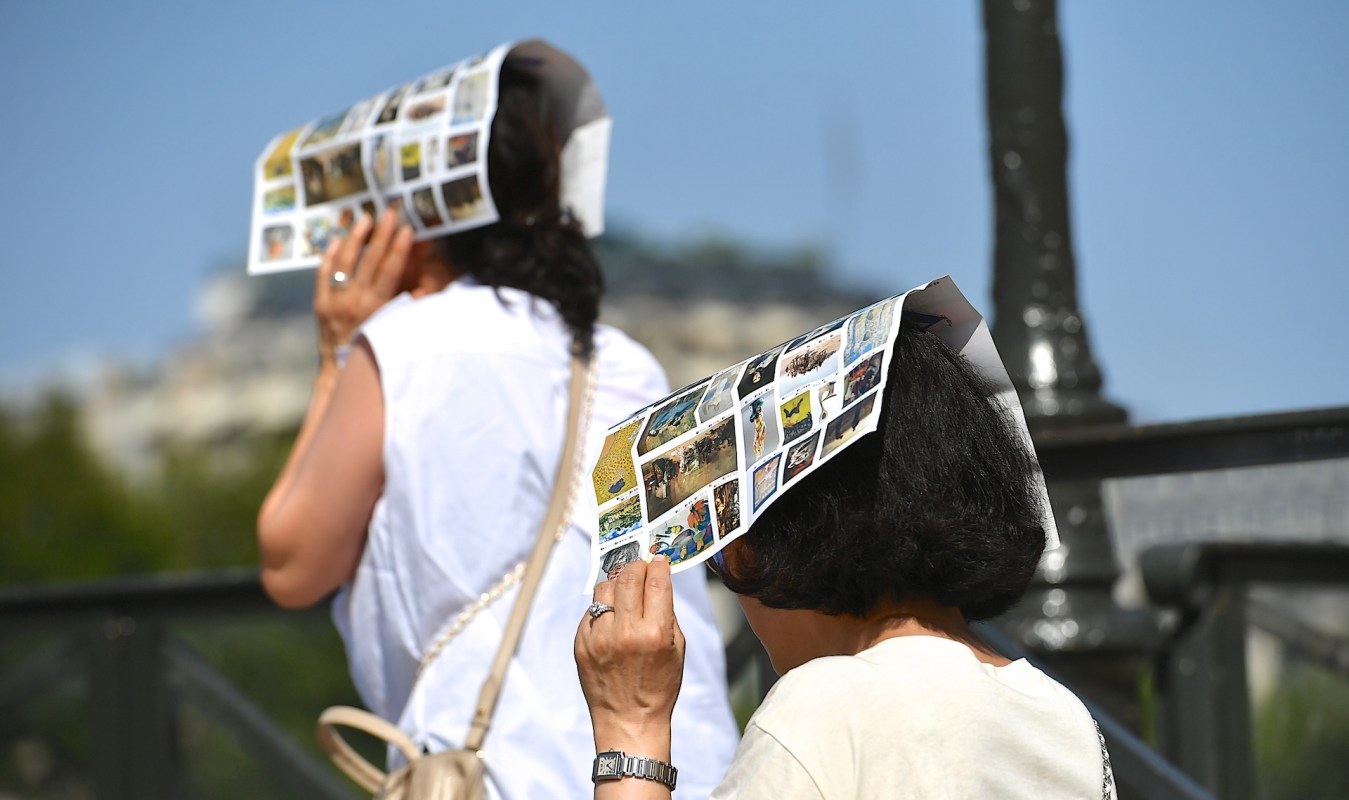 Two women walking outdoors wearing colorful picture-covered hats to shield themselves from the sun.