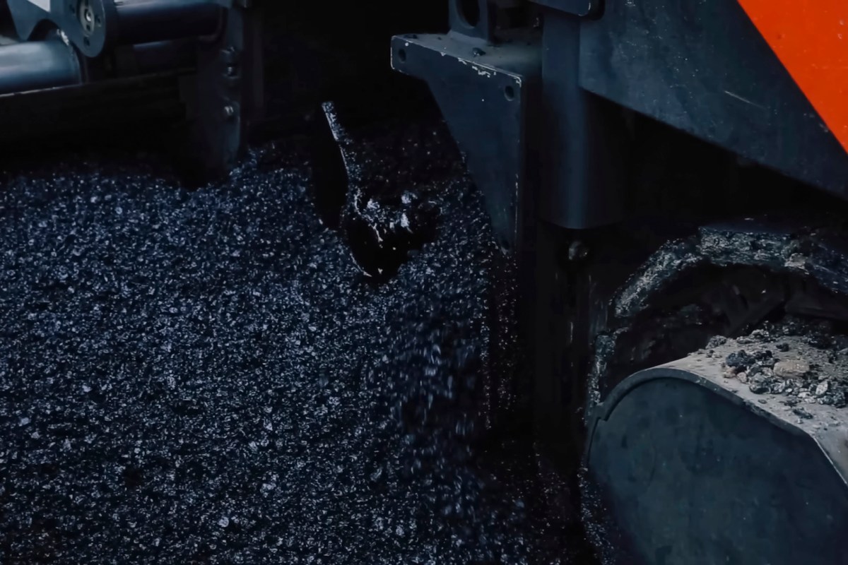 An asphalt paving machine pouring black asphalt onto the ground.