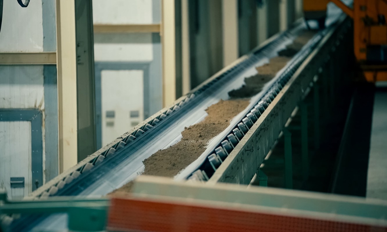 A conveyor belt transporting a layer of clay in an industrial setting.