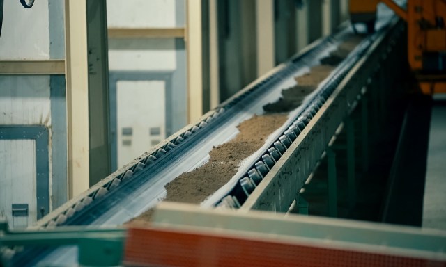 A conveyor belt transporting a layer of clay in an industrial setting.