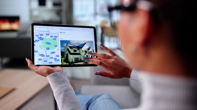 A person examines a real estate listing on a tablet, featuring a map and a house image.