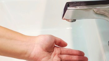 A hand positioned under a faucet, with no water coming out.