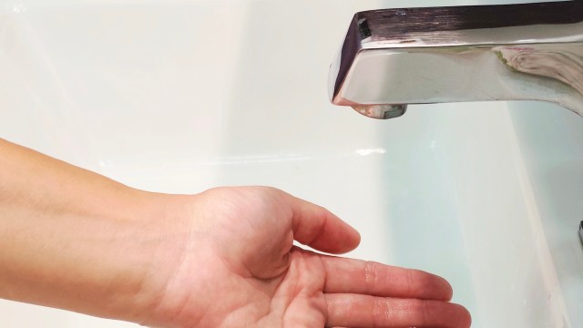 A hand positioned under a faucet, with no water coming out.