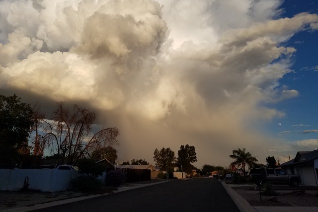A dramatic sky filled with billowing clouds and light rain, viewed from a residential neighborhood street.