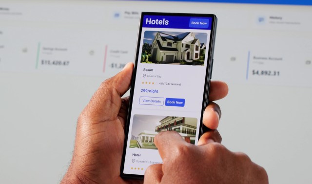 A person using a smartphone to browse hotel options on a travel app, featuring two listings and booking options.