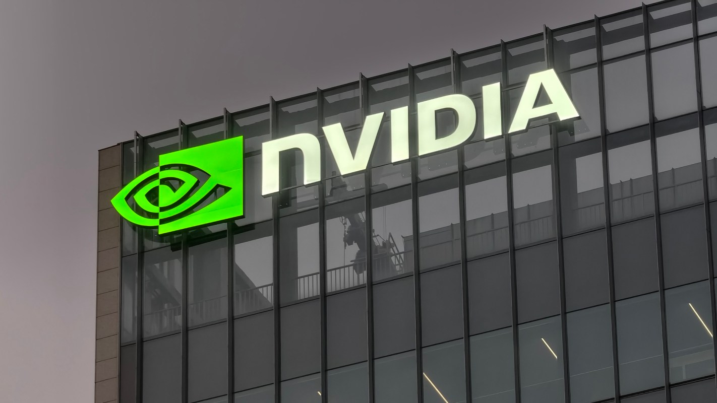 The illuminated NVIDIA logo on a modern glass building against a gray sky.