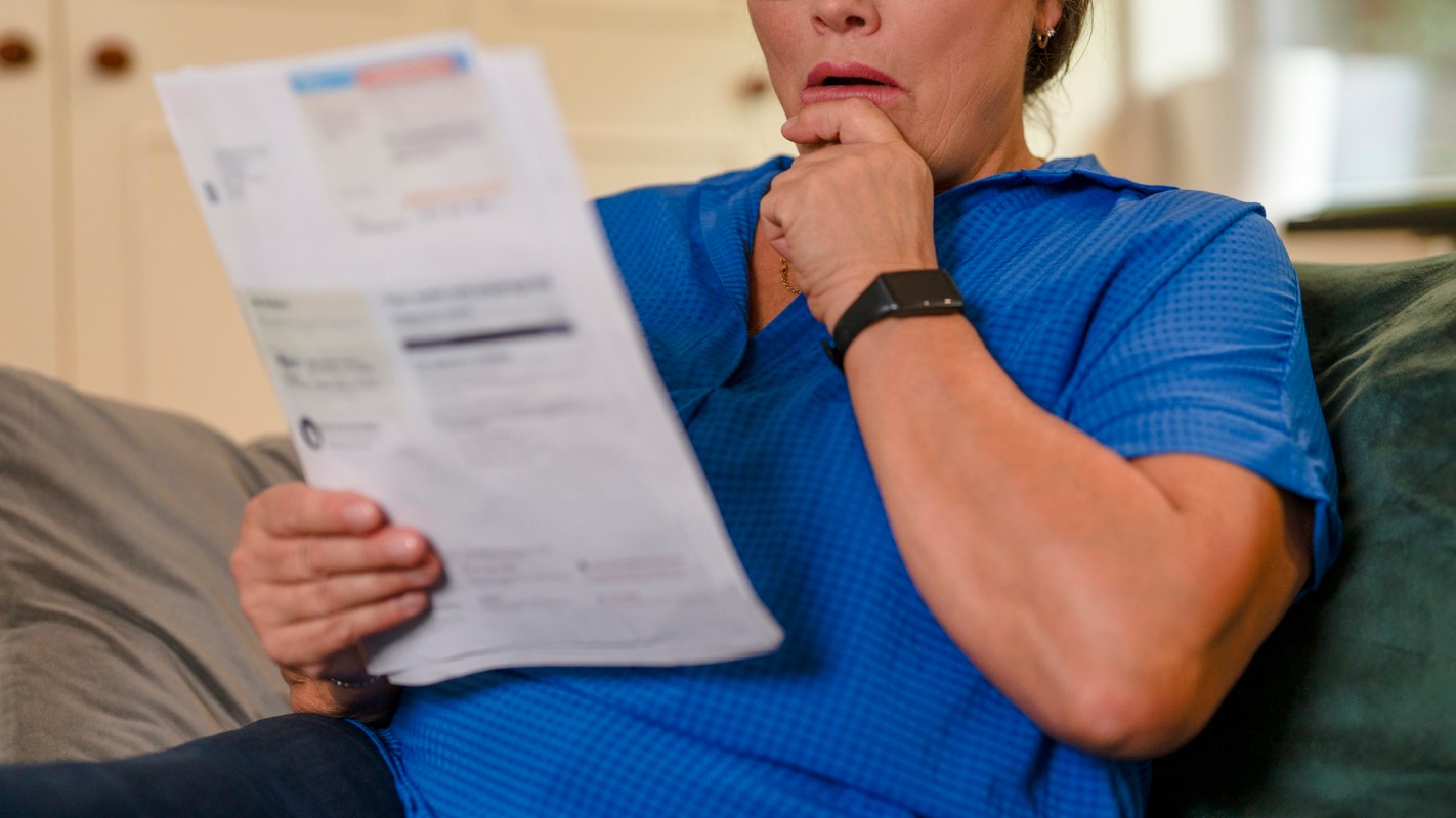 A woman in a blue shirt looks concerned while reading a document on a couch.
