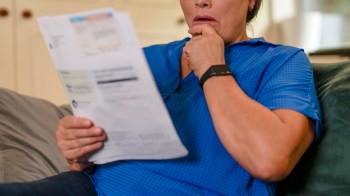 A woman in a blue shirt looks concerned while reading a document on a couch.