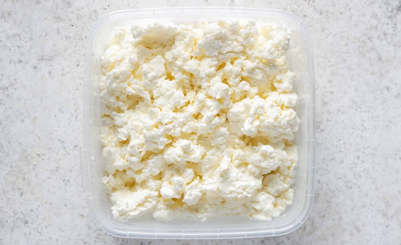 A container of fluffy, white cottage cheese on a light surface.