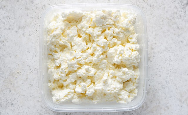 A container of fluffy, white cottage cheese on a light surface.