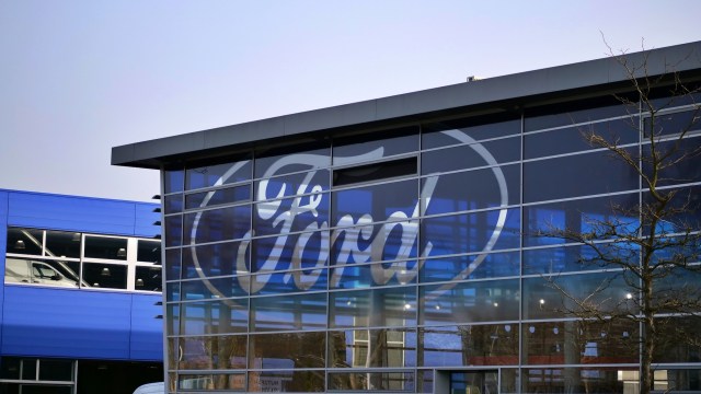 A close-up of a modern building facade featuring the Ford logo reflected in large glass windows.