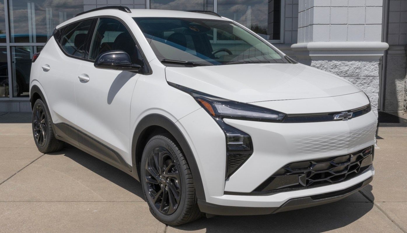 A white Chevrolet Bolt SUV with black wheels parked outside a dealership on a sunny day.