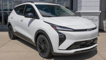 A white Chevrolet Bolt SUV with black wheels parked outside a dealership on a sunny day.