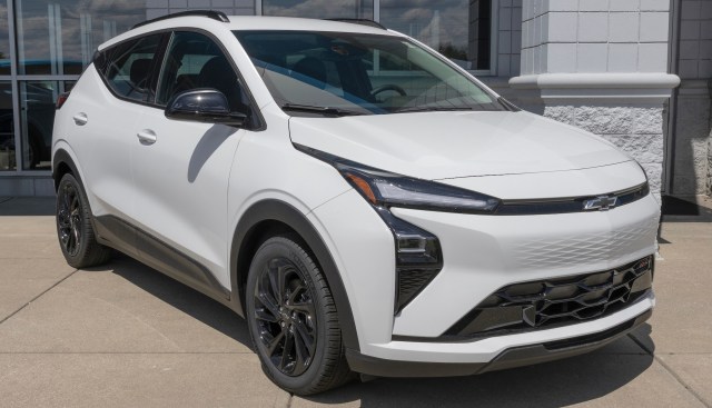 A white Chevrolet Bolt SUV with black wheels parked outside a dealership on a sunny day.