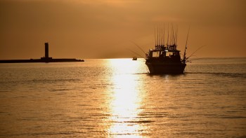 A fishing boat and lighthouse silhouetted against a golden sunset.