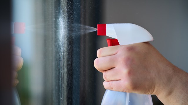 A hand using a spray bottle to mist a glass surface.