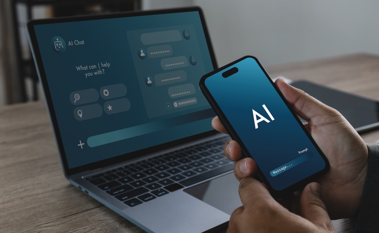 A person holds a smartphone displaying an AI chat interface next to a laptop showing a similar chat application.