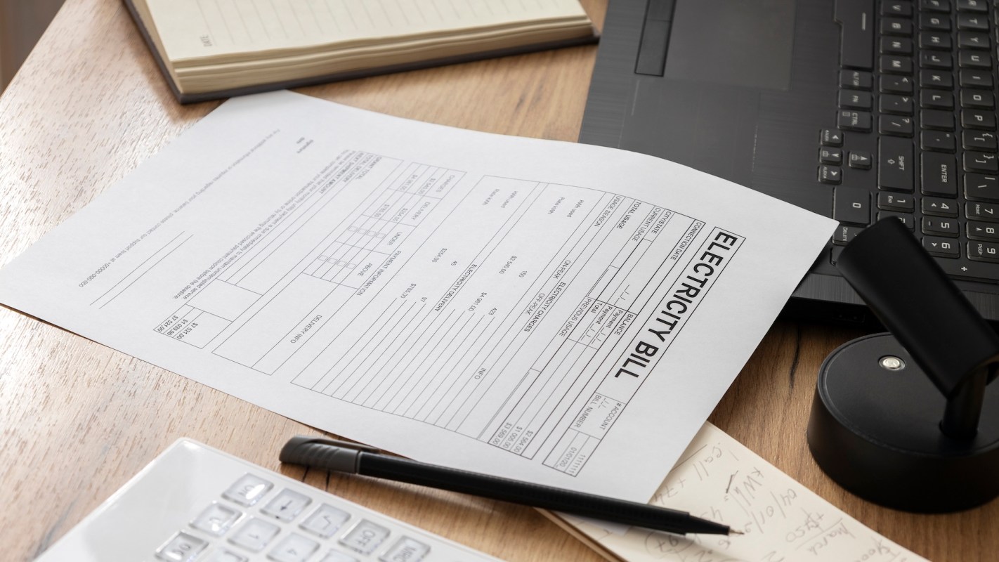 An electricity bill beside a laptop, pen, and calculator.