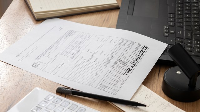 An electricity bill beside a laptop, pen, and calculator.