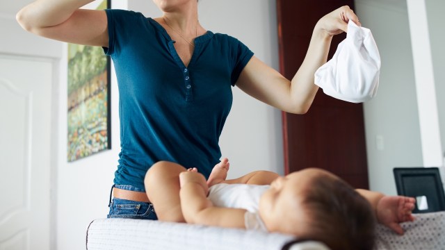 A woman holding a diaper while changing a baby on a changing table.