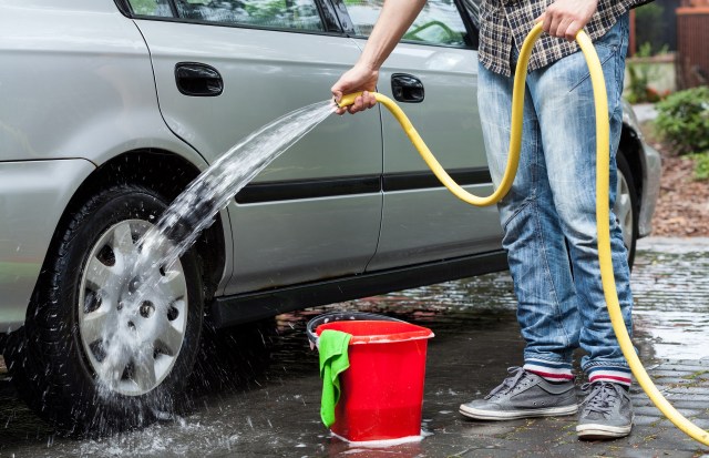 A person using a bucket of soapy water and a hose to wash a car.