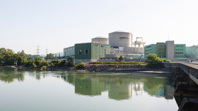 A nuclear power plant with large cooling towers reflecting in a calm river under a clear sky.