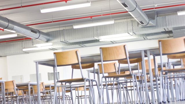 A modern, empty classroom with metal chairs arranged around tables and exposed ductwork on the ceiling.