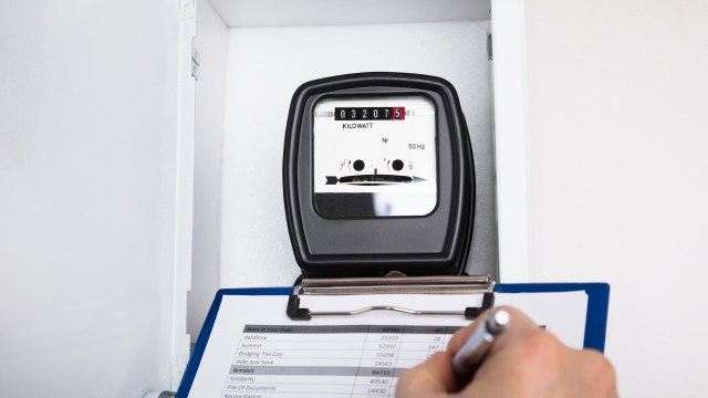 A close-up of an electric meter displaying kilowatt usage and a clipboard with a document.