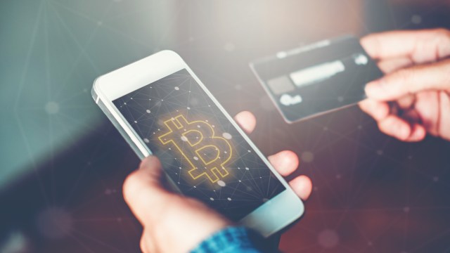 A person holding a smartphone displaying a Bitcoin symbol and a credit card in the other hand.