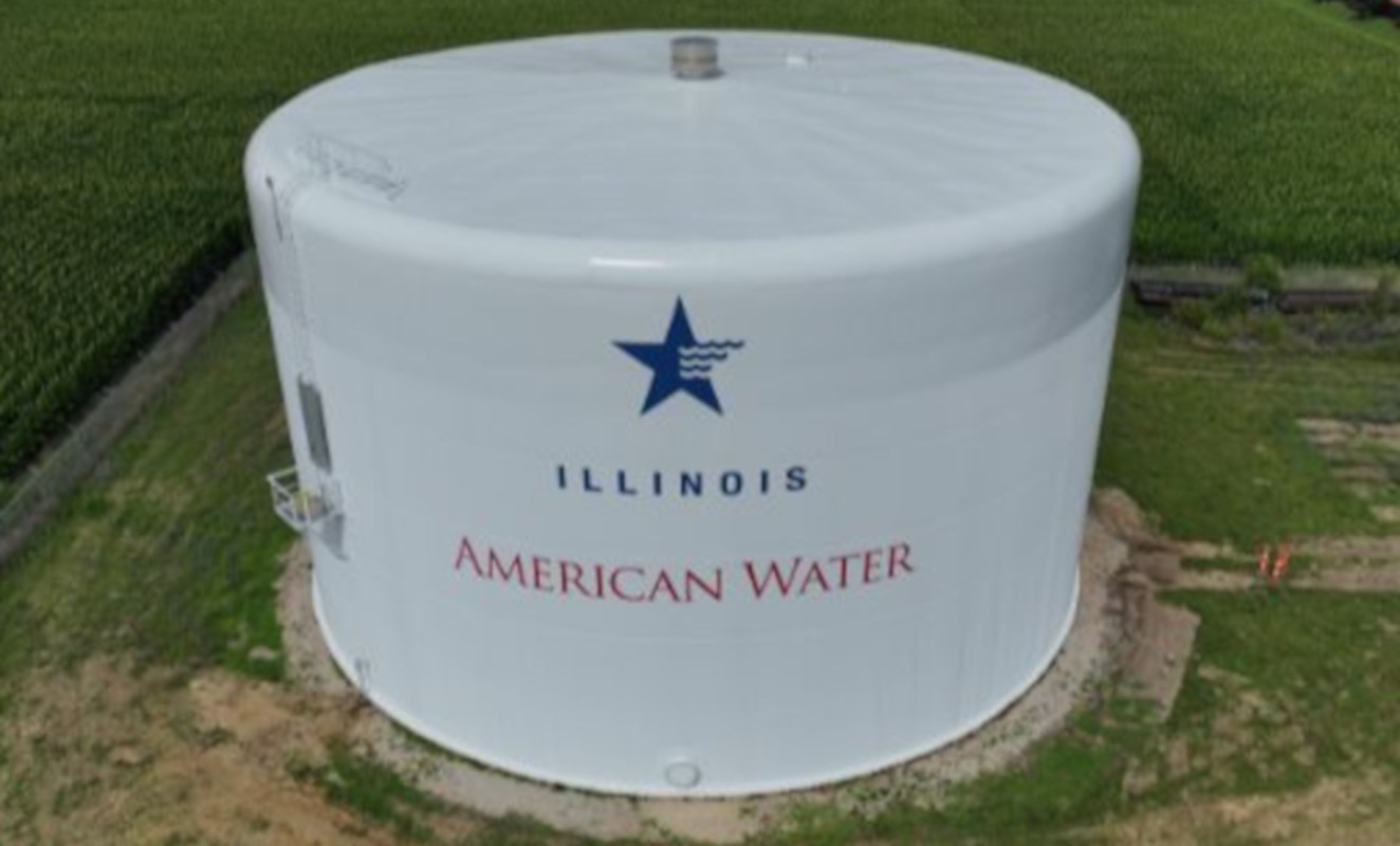 A large white water tower labeled "Illinois American Water" surrounded by green fields.