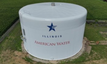 A large white water tower labeled "Illinois American Water" surrounded by green fields.