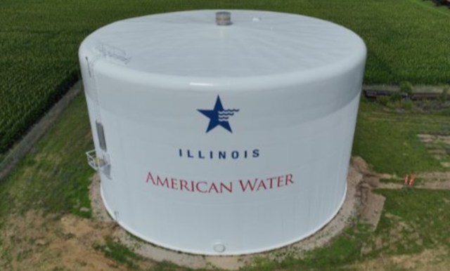 A large white water tower labeled "Illinois American Water" surrounded by green fields.
