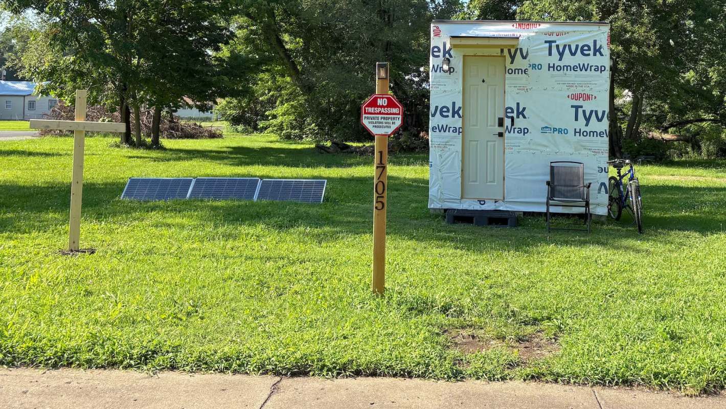 An unfinished tiny home next to solar panels.
